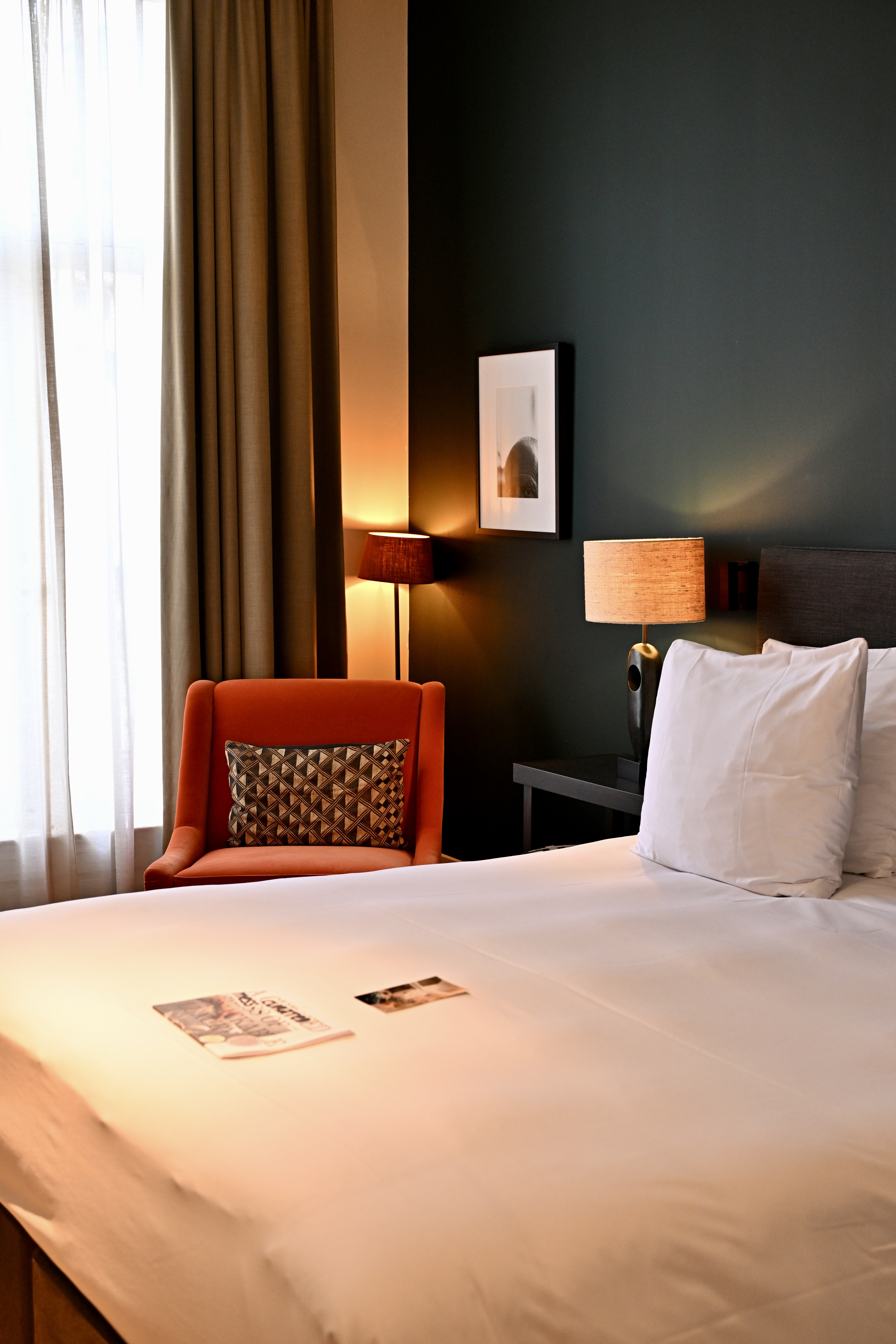Hotel FRANQ bedroom with a white bed, green wall and orange armchair