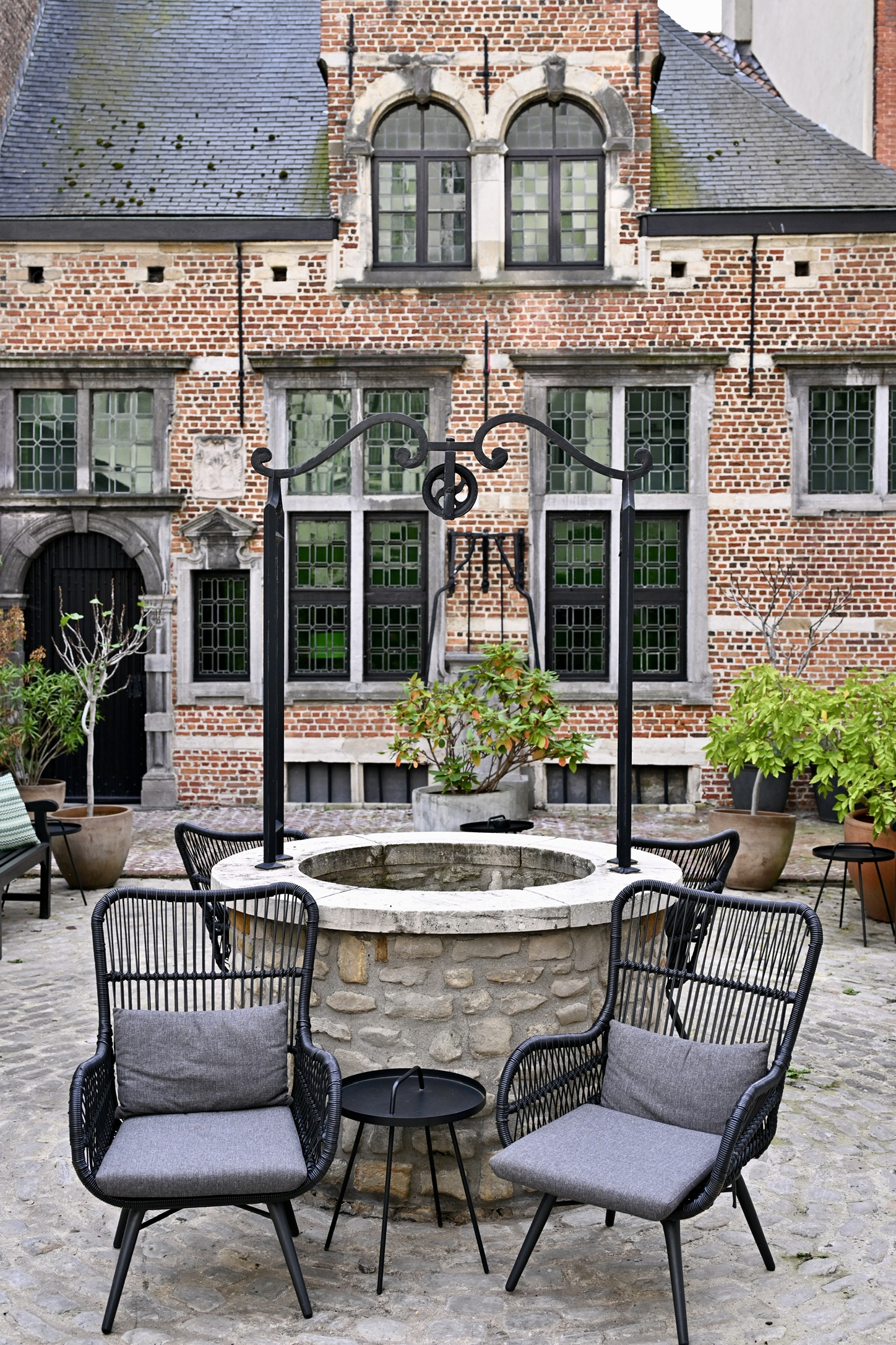 Hotel FRANQ’s paved courtyard with a stone well and the brick façade of Den Doorenboom