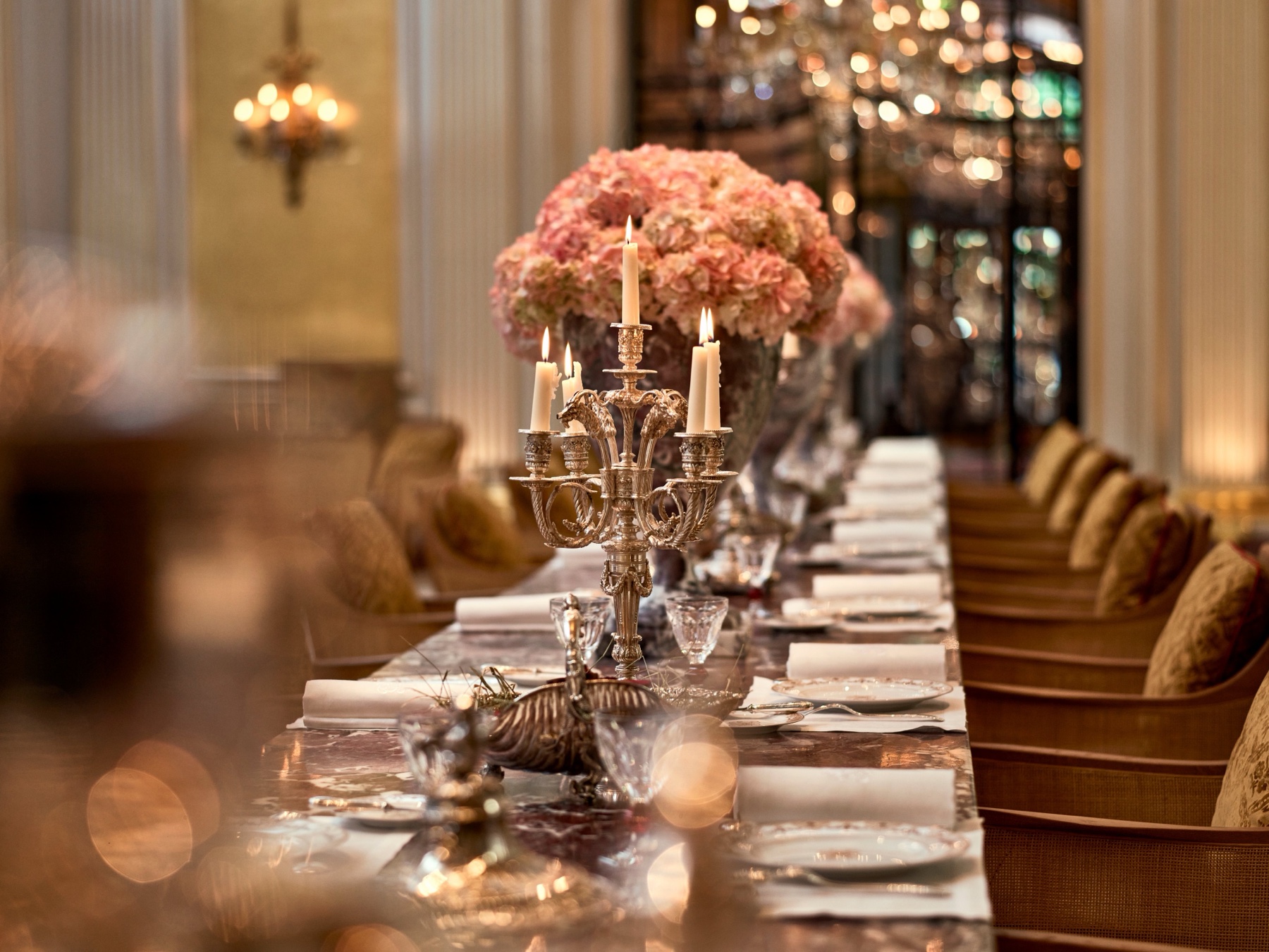 Vue d’archive de la longue table en marbre rose dressée de chandeliers en argent, de serviettes blanches et de fleurs roses dans la salle gastronomique de l’Hôtel Plaza Athénée