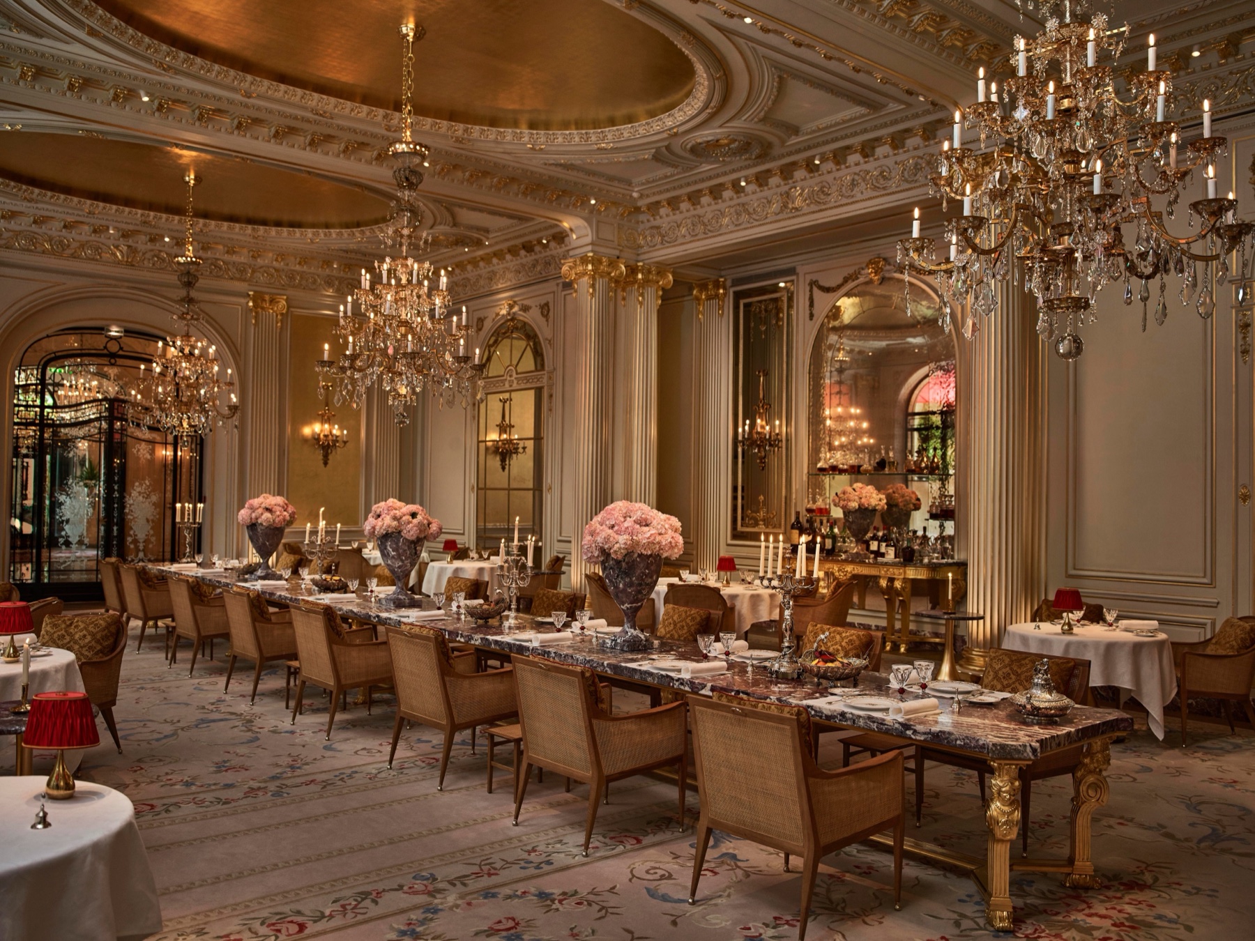 Vue d’ensemble de la salle de Rémi Tessier à l’Hôtel Plaza Athénée, avec sa longue table en marbre rose, ses lustres et son plafond doré